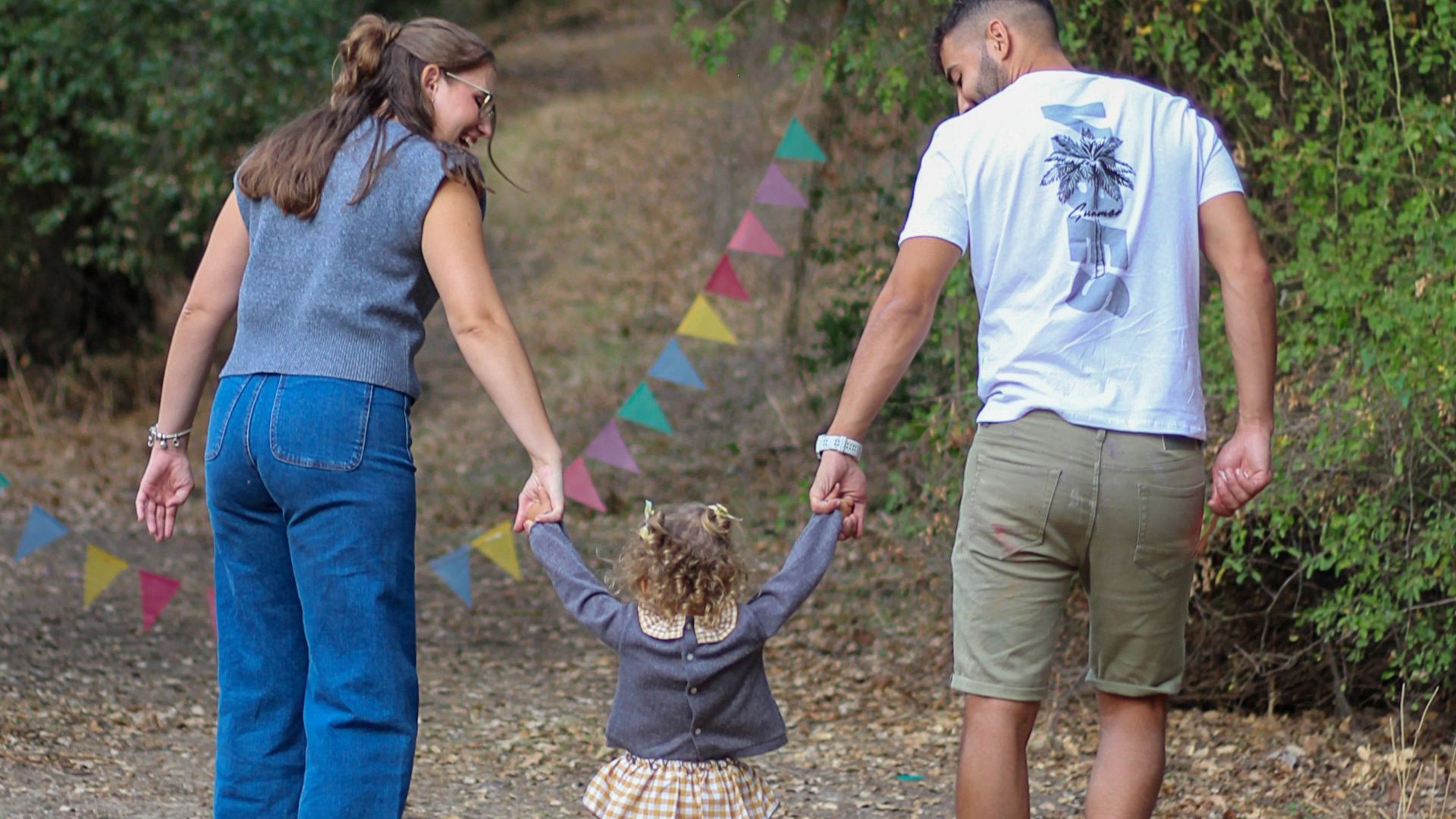  Madre y padre acompañan a una niña de la mano durante un paseo por la naturaleza.