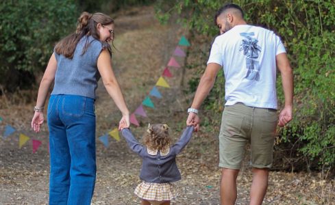  Madre y padre acompañan a una niña de la mano durante un paseo por la naturaleza.