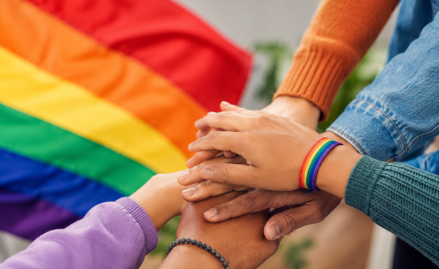  Imagen realizada con IA que muestra varias manos juntas en señal de amistad con una bandera arco iris de fondo